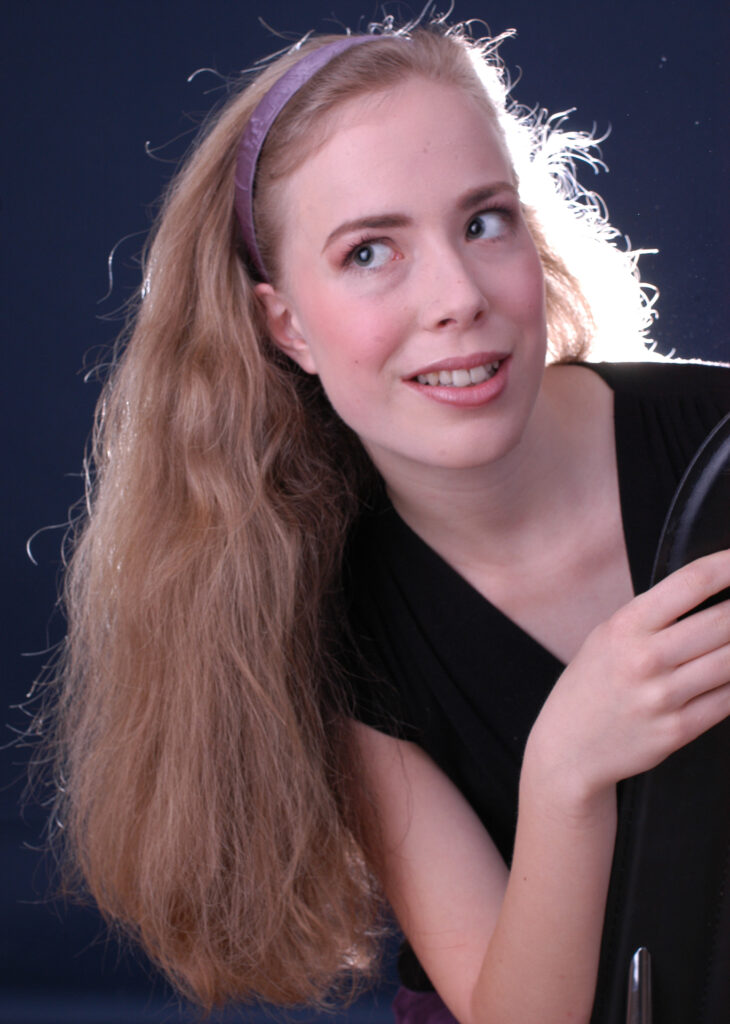 Komparsen Sedcard vom Fotostudio Belichtungswert München, junges Talent mit langen blonden Haaren, violettem Kopfband, schwarzem Outfit und seitlichem Blick
