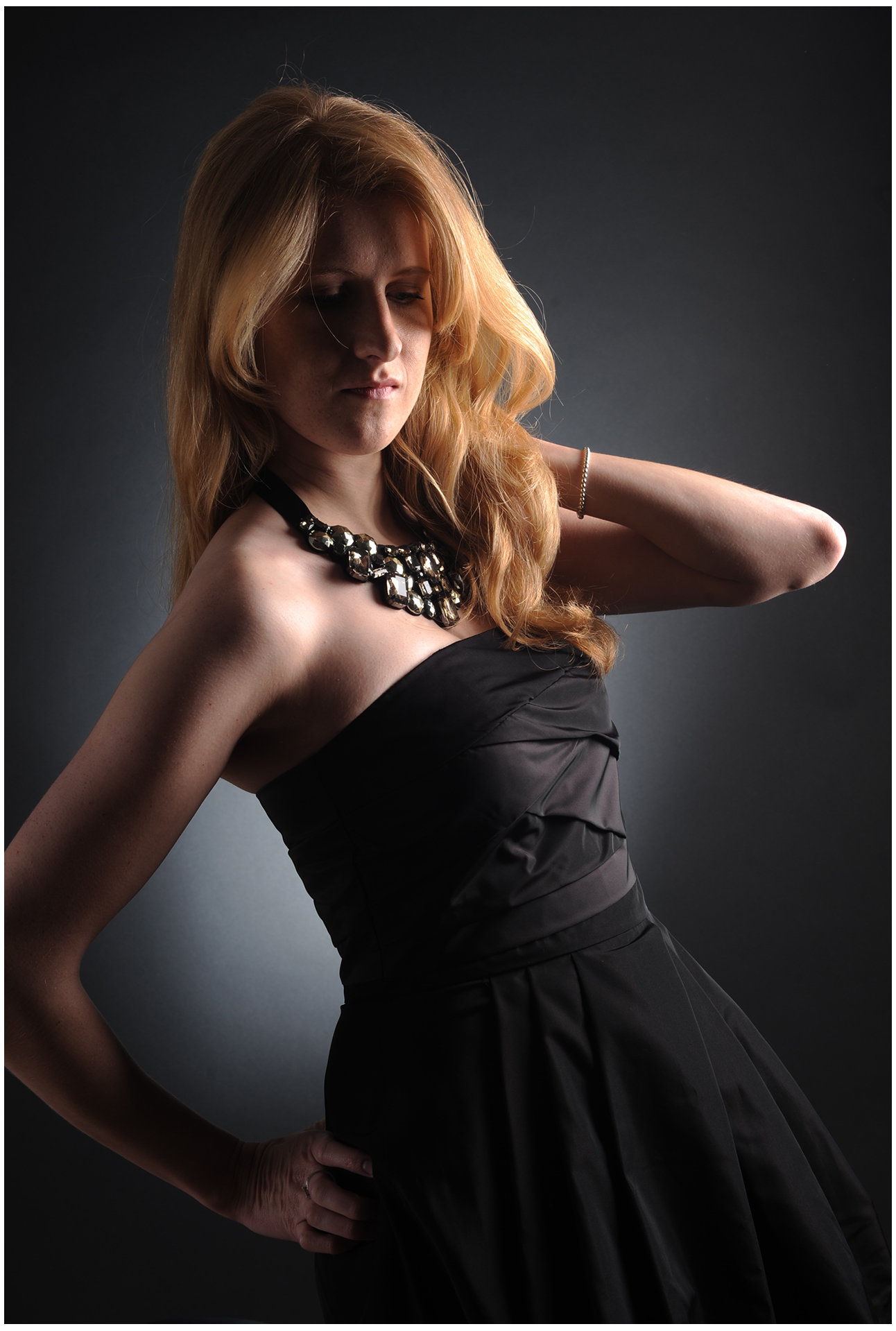 Komparsen Sedcard Fotoshooting im Fotostudio Belichtungswert München, junge Frau in schwarzem Kleid vor dunklem Hintergrund mit dramatischem Licht und seitlicher Pose