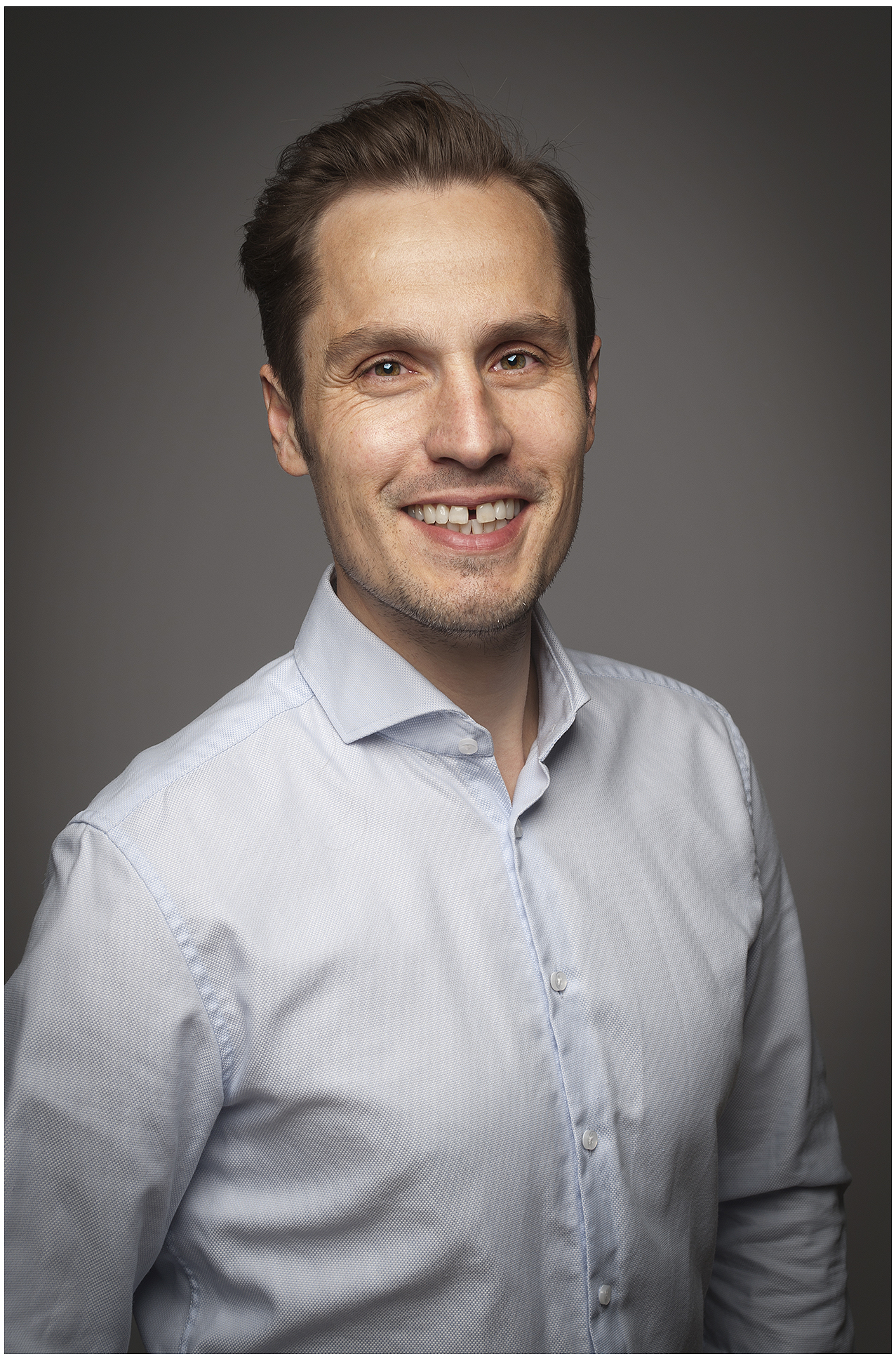 legere-businessfoto-mann-laechelnd-hellblaues-hemd-professionell-studio-dunkler-hintergrund
