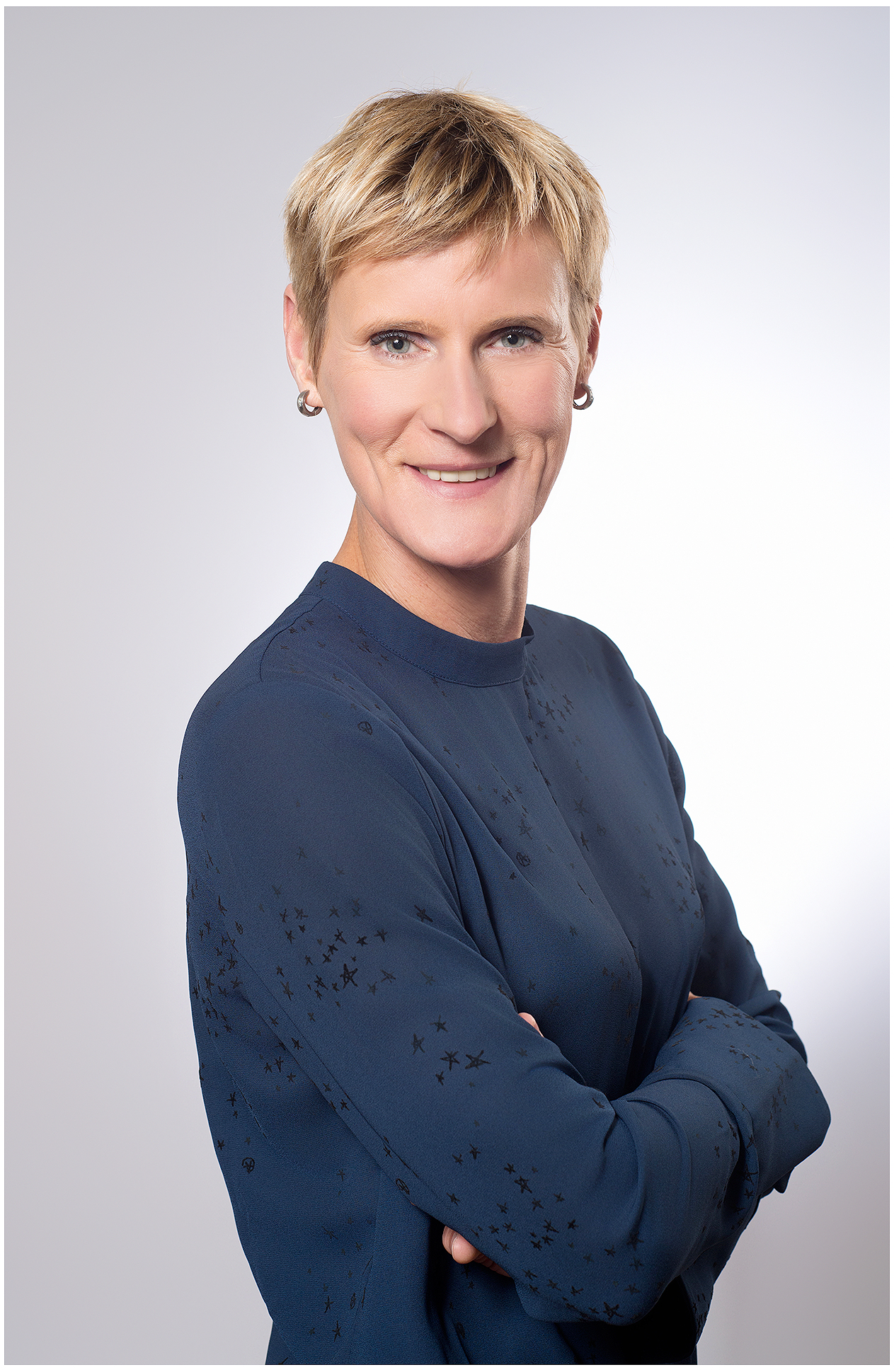 modernes-linkedin-headshot-businessportrait-frau-mit-kurzhaarschnitt-im-blauen-oberteil-laechelt-vor-neutralem-studiohintergrund