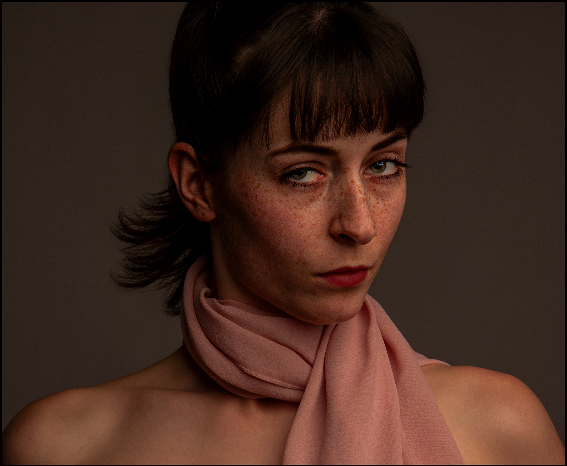 Beauty Portrait für Model Sedcard im Fotostudio Belichtungswert München, junge Frau mit kurzem dunklem Haar, Sommersprossen und rosa Schal blickt seitlich ausdrucksstark in dramatischem Studiolicht
