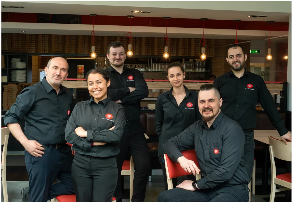 Mitarbeiter der Schnell-Food Restaurant, alle uniformiert, lächelnd in die Kamera, in Hintergrund einer Bar