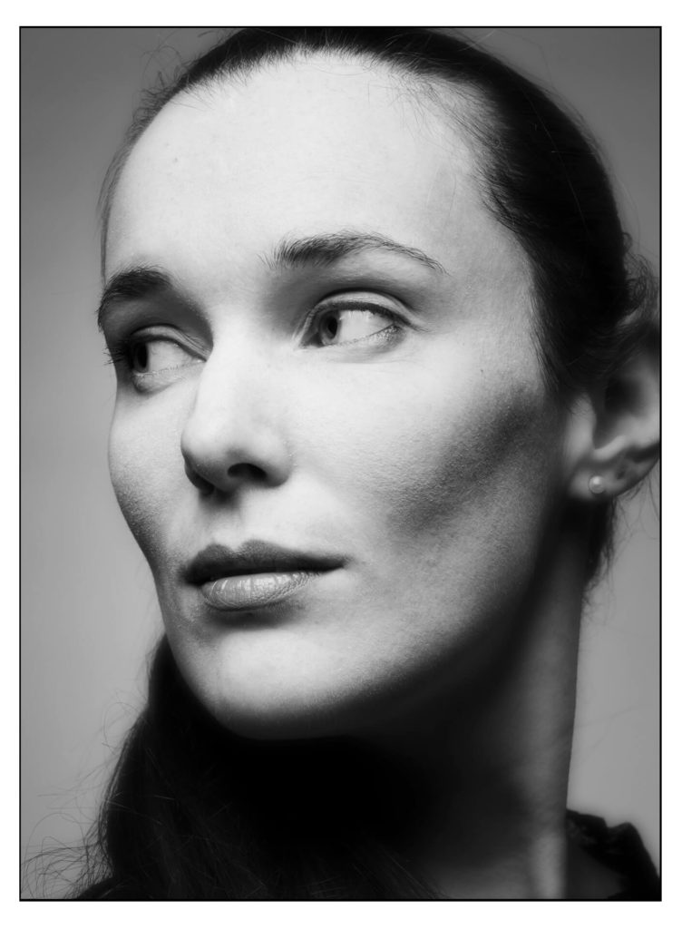 Portrait Fotoshooting München im Fotostudio Belichtungswert, Schwarz-Weiß Headshot einer jungen Frau mit seitlichem nachdenklichem Blick und weichem Studiolicht