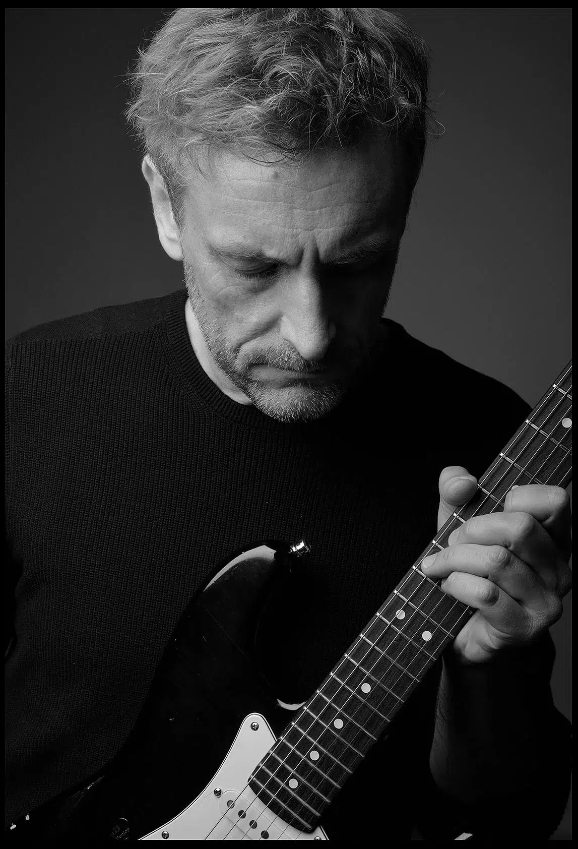 Portrait eines Musikers innen im Studio, stehend. im schwarzen Hemd mit der Gitarre, schwarz-weiß
