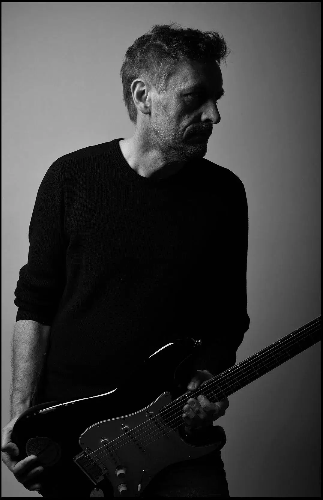 Portrait eines Musikers innen im Studio, stehend. im schwarzen Hemd, mit e-Gitarre schwarz-weiß