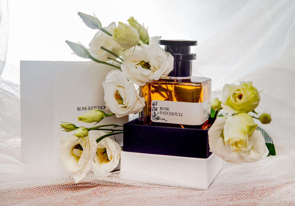 Hochwertige Produktfotografie von Rose Patchouli Parfüm mit elegantem Flakon, weißer Geschenkbox und weißen Blüten auf hellem Hintergrund