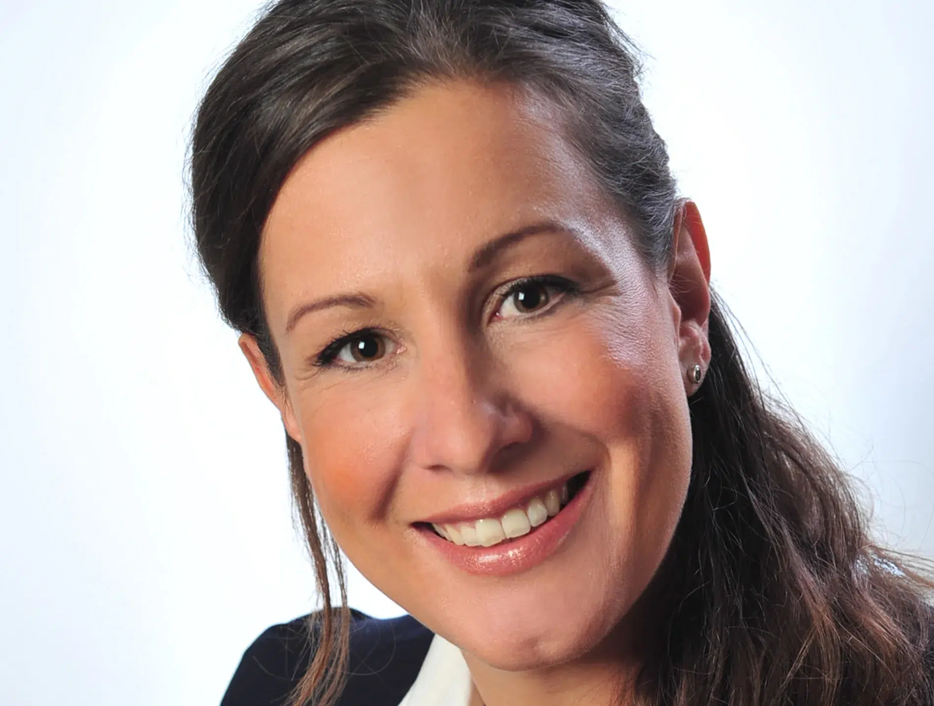 Portrait einer lächelnden Frau mit langen, braunen Haaren in weißer Bluse und dunkelblauem Blazer, vor hellem Hintergrund