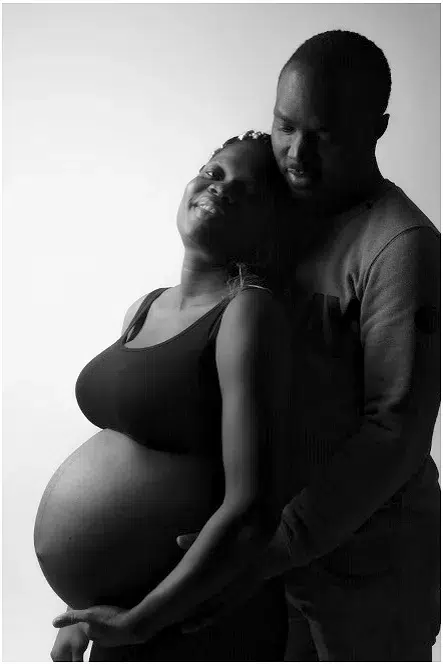 Ein Paar stehend, Frau schwanger, der Mann dahinter, schwarz-weiss beim Babybauch Fotoshooting
