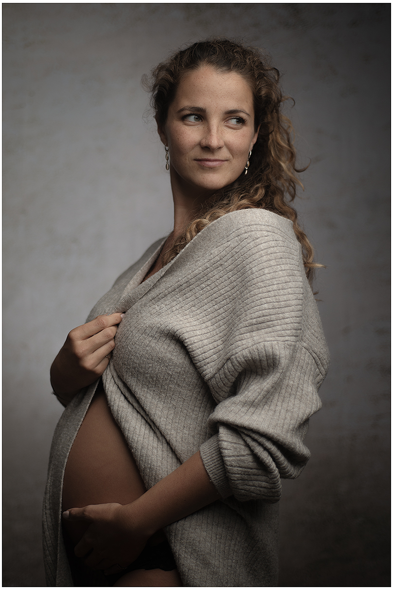 Frau mit Babybauch posiert für Portrait in Pullover, schaut leicht zur Seite
