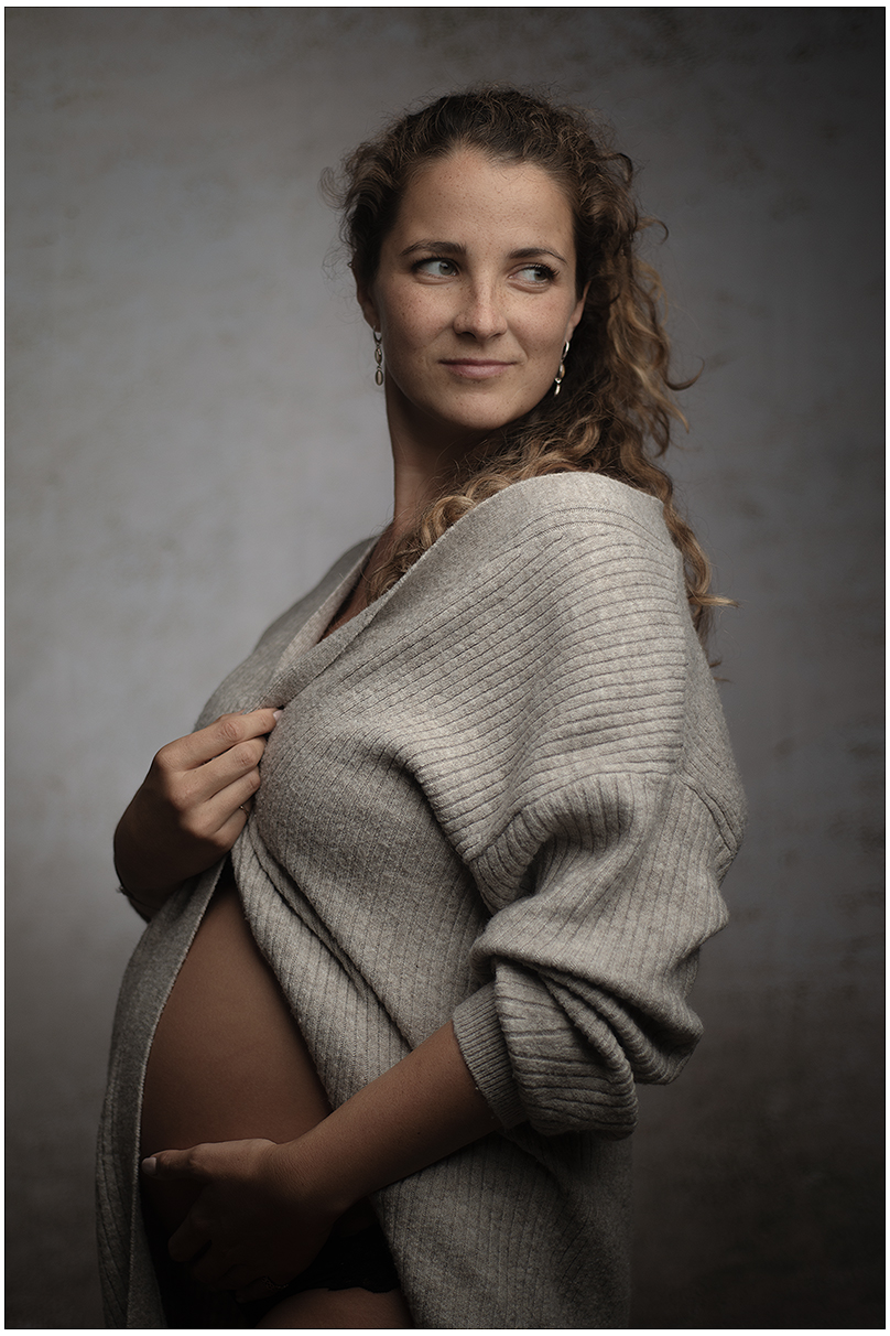 Frau mit Babybauch posiert für Portrait in Pullover, schaut leicht zur Seite