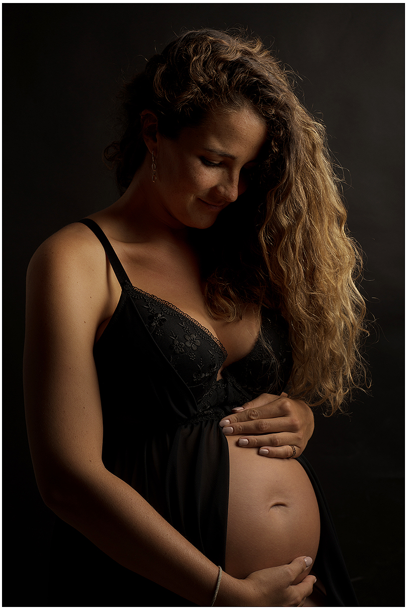 Eine schwangere Frau in einem schwarzen Kleid und schwarzen BH. Die Frau hat einen deutlich sichtbaren Babybauch.